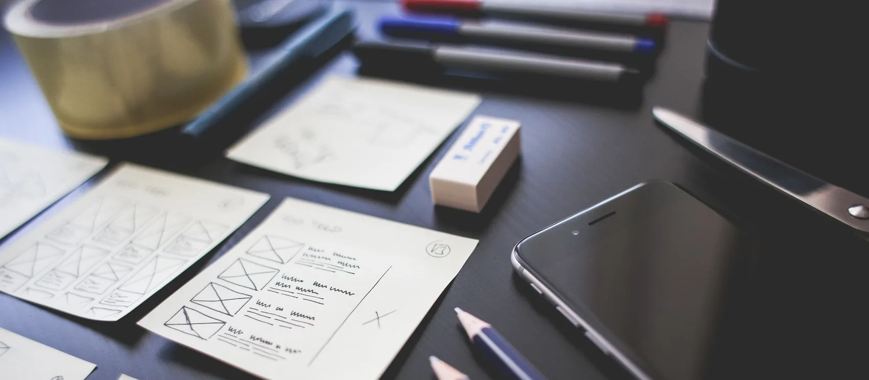 Bocetos de wireframes de una aplicación móvil sobre un escritorio junto a lápices y un teléfono.
