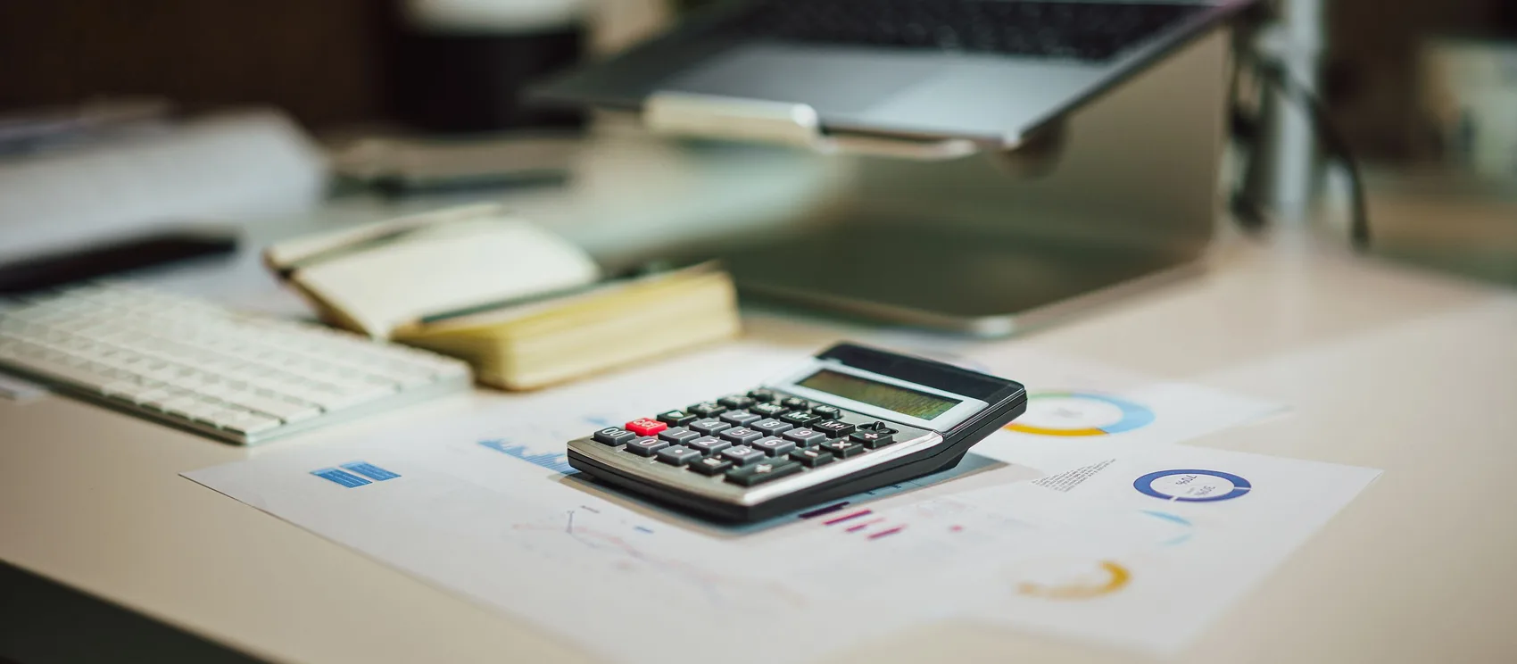 Calculadora sobre reportes financieros junto a una laptop en el escritorio de un despacho contable
